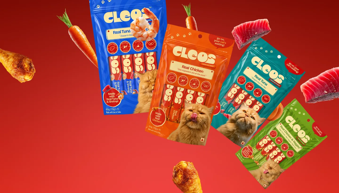 Cleos cat treat pouches floating with fresh chicken, tuna and carrots on a red background
